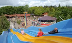 Familienrutsche im Tolk-Schau Freizeitpark mit Menschen, die rutschen und Karussell.