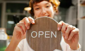 Frau hält ein Holzschild mit der Aufschrift "OPEN" in einem Café.